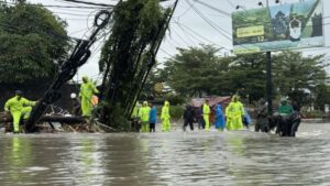 Petugas dan warga bergotong royong memindahkan halte bus serta tiang kabel komunikasi yang roboh dan menghalangi jalan akibat banjir di depan Mako Brimob Polda Bali, Rabu (10/09/2025) (Foto : Detik.com)