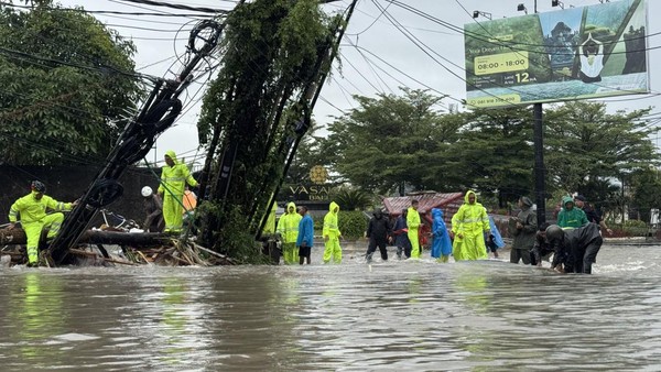Petugas dan warga bergotong royong memindahkan halte bus serta tiang kabel komunikasi yang roboh dan menghalangi jalan akibat banjir di depan Mako Brimob Polda Bali, Rabu (10/09/2025) (Foto : Detik.com)